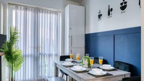 A dining area with a table set for four, a potted plant, and a view of the outside through a window with blinds. - Home Near City Centre, Pets Welcome, Parking (Manchester)