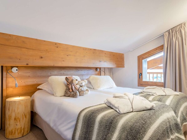 Une chambre d’hôtel avec une tête de lit en bois, une grande fenêtre avec des rideaux, une lampe de chevet et un lit recouvert d’une couverture à rayures.