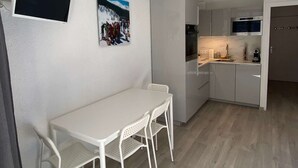 A compact kitchen with white cabinets, a built-in oven, and a microwave. There is a small dining area with a white table and chairs.