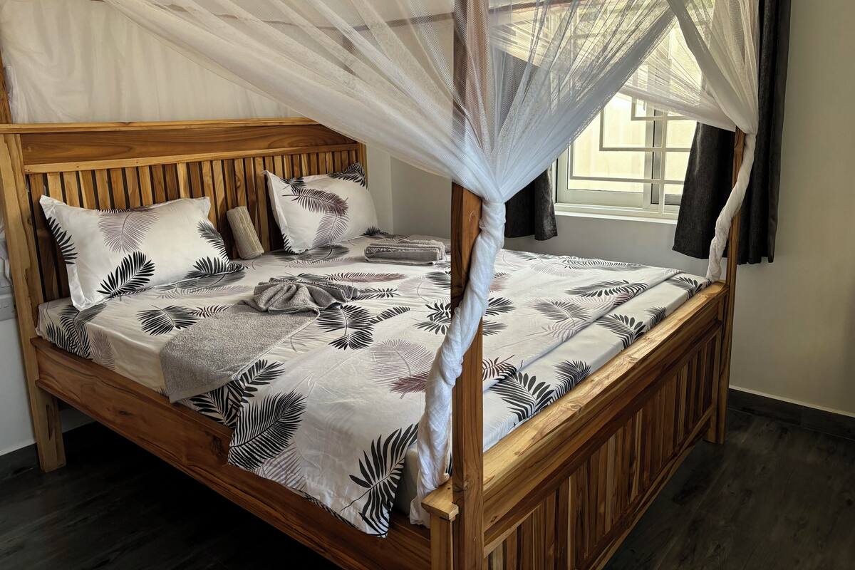 A wooden bed with a canopy, a patterned bedspread, and pillows with a leaf design.