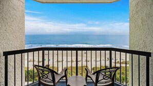A balcony with two chairs and a table, overlooking a beach with waves and a clear sky. - Compass Cove Resort Unit 662 - Oceanfront (Myrtle Beach)