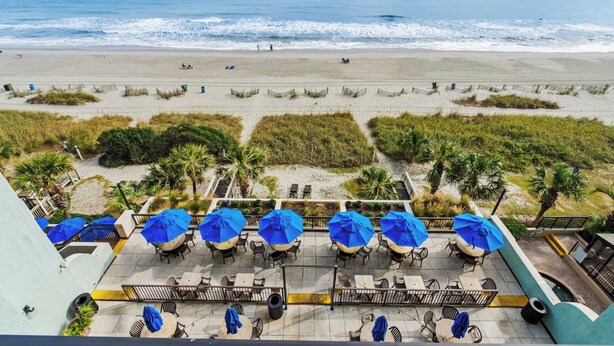 A beachside patio with outdoor seating and umbrellas, overlooking the ocean. - Compass Cove Resort Unit 662 - Oceanfront (Myrtle Beach)