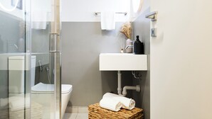 Et moderne badeværelse med brusekabine i glas, toilet og håndvask med hvid bordplade.