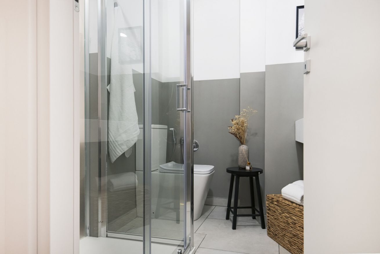 A modern bathroom with a glass shower enclosure, a toilet, and a small table with a vase.