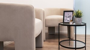 Et rum med en beige sofa, et lille rundt bord med en billedramme og en plante, og en lyseblå væg.
