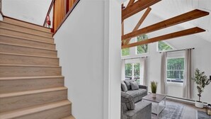 Eine Treppe mit Holzdielen führt zu einem Wohnbereich mit grauem Sofa, Couchtisch und einer Pflanze.