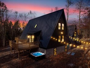 Situated in a wooded area, this cabin features a deck with a hot tub and string lights.