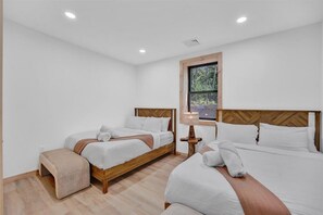 Two single beds with wooden headboards and white bedding, a nightstand with a lamp, and a small bench.