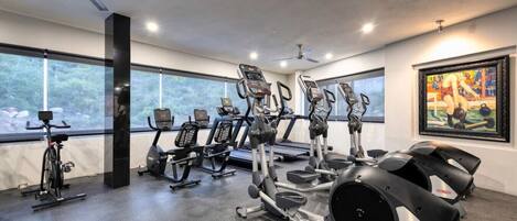 A gym with various exercise machines, large windows, and a ceiling fan.