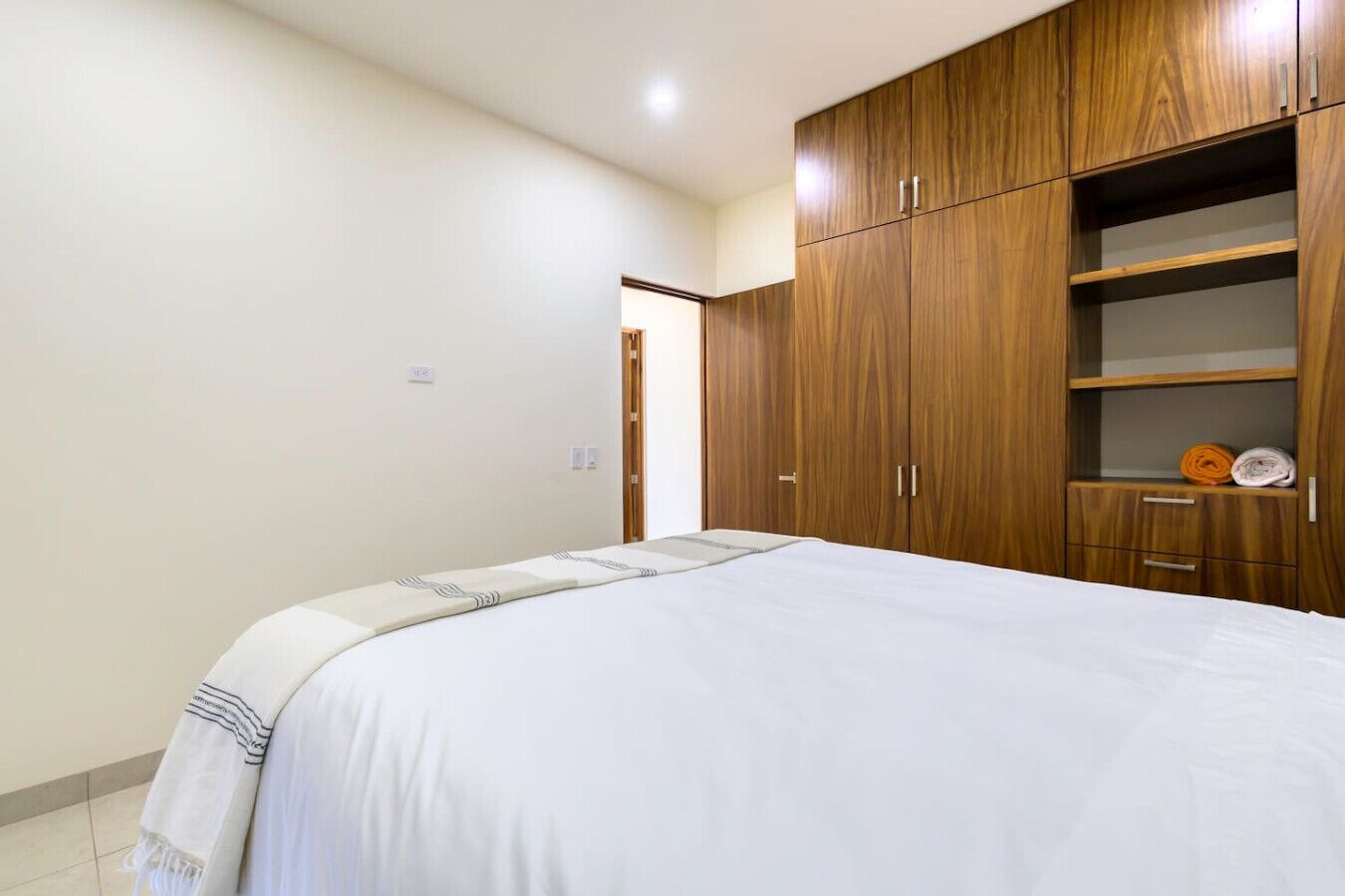 A bedroom with a large bed, wooden wardrobe, and a small shelf with folded towels.