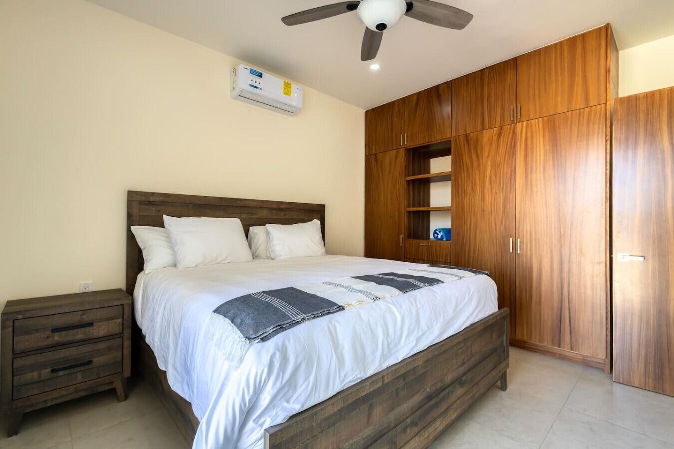 Un dormitorio con cama, armario de madera, mesita de noche y ventilador de techo.
