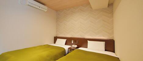 A hotel room with two single beds, a wooden headboard, a nightstand with a phone, and a wall-mounted air conditioner.