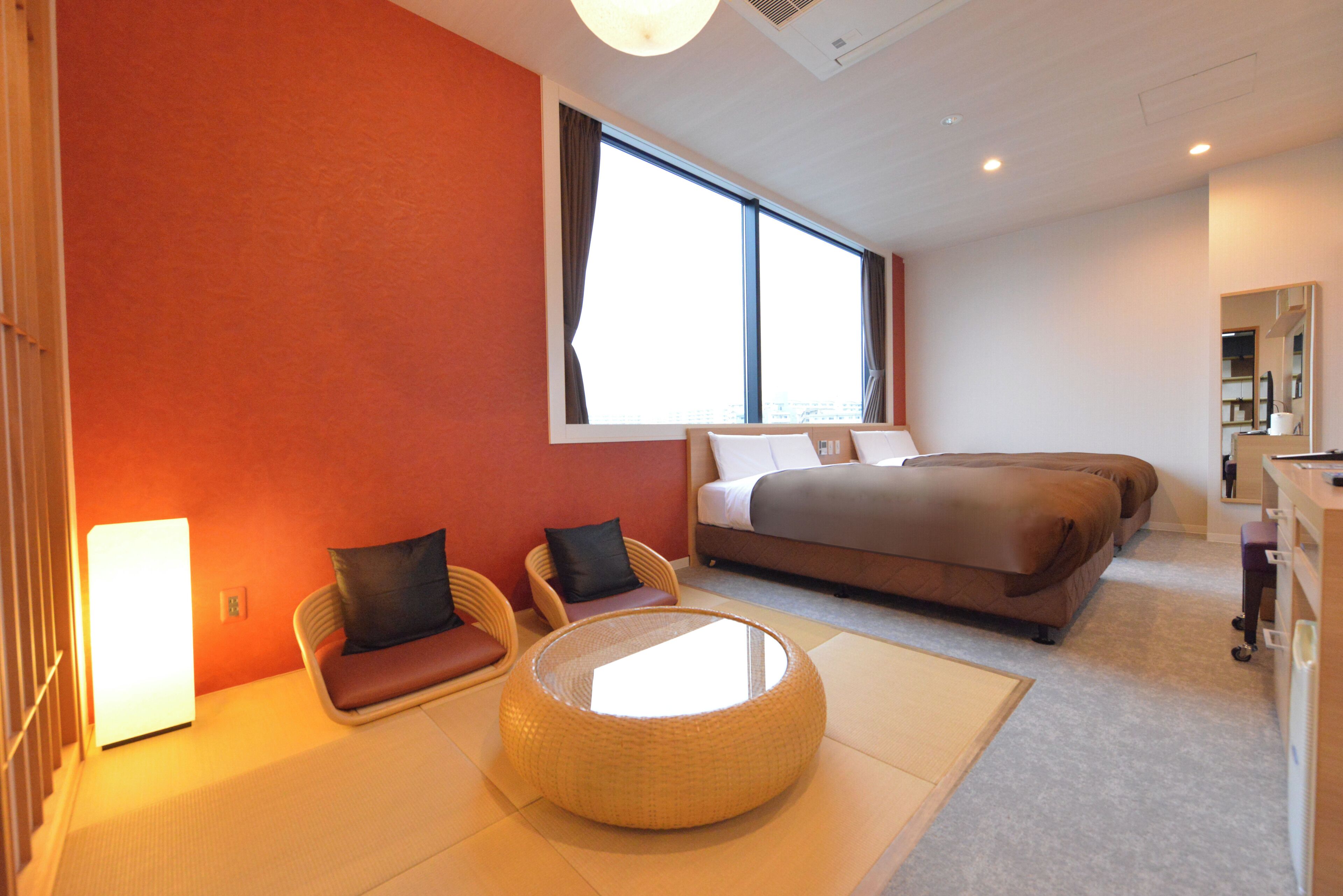 A modern hotel room with a large bed, two chairs, a round table, and a large window.
