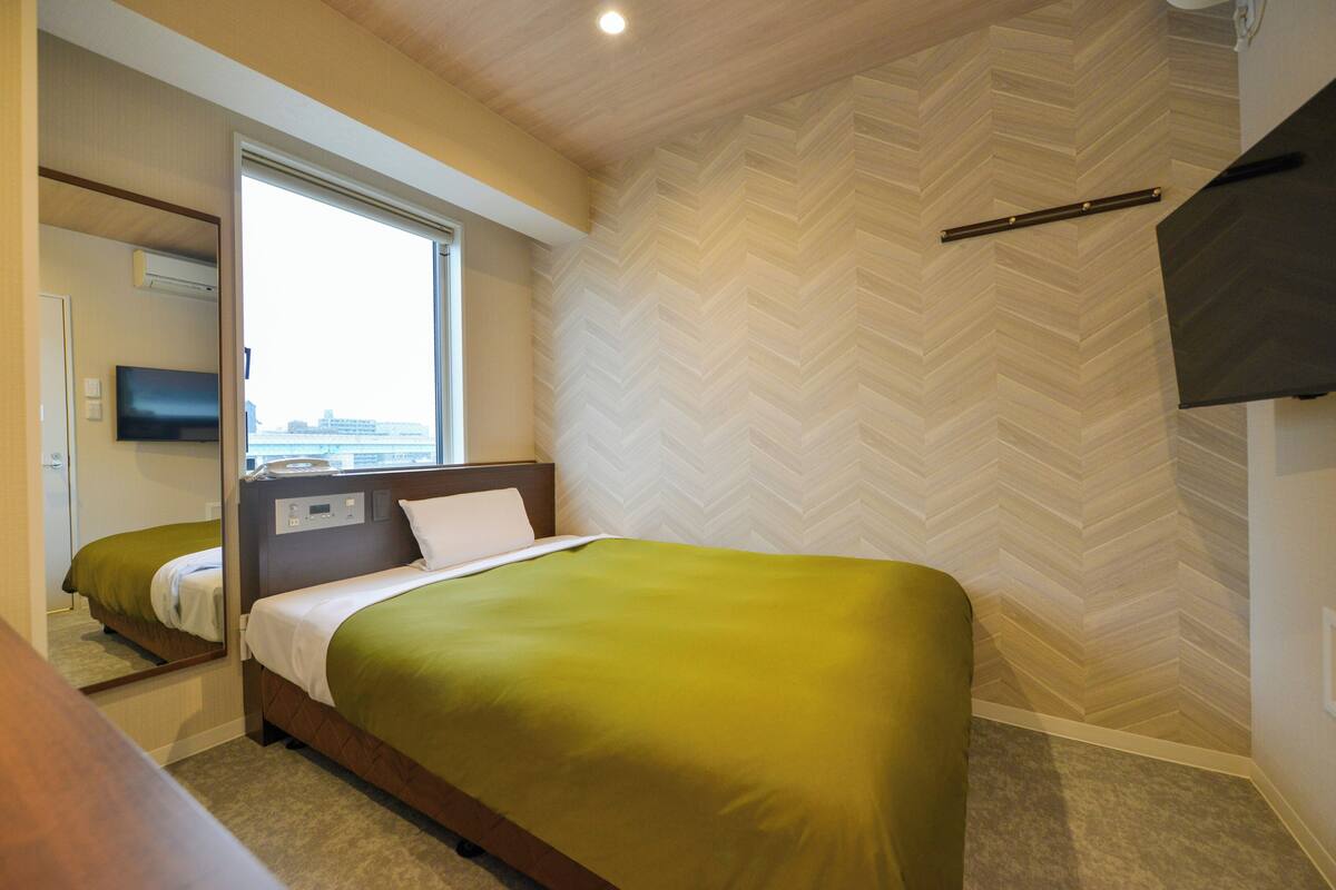 Una habitación de hotel con una cama, televisión y ventana con vistas.
