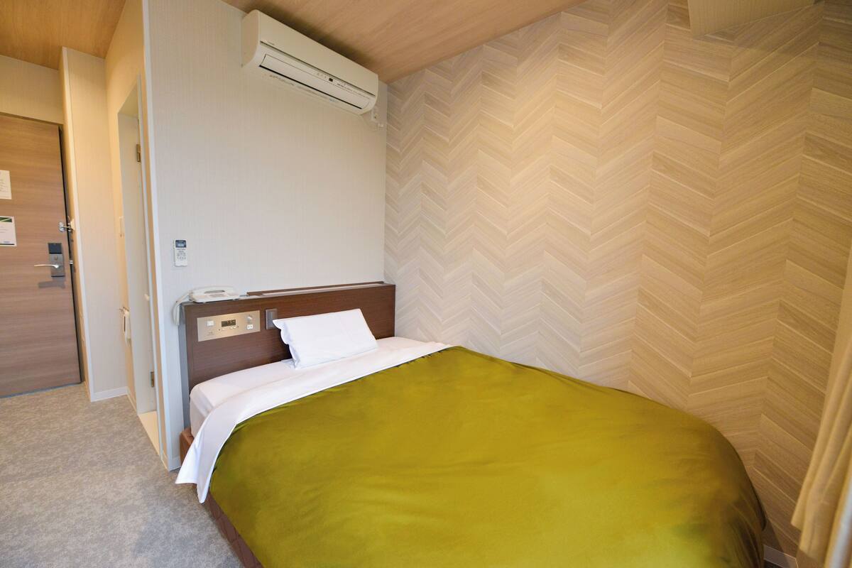 Habitación de hotel con cama, unidad de aire acondicionado, puerta de madera y pared con motivo de espiga.