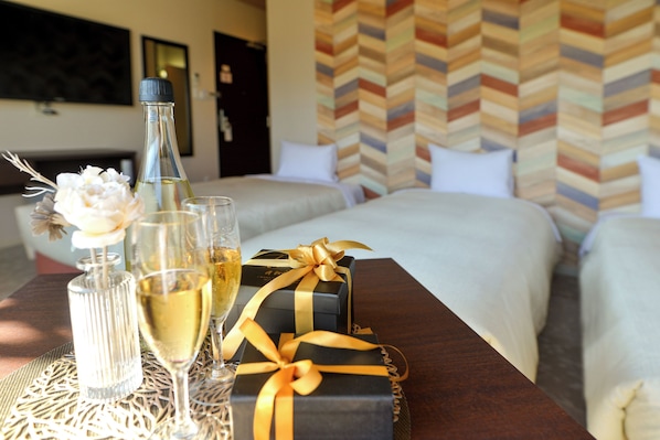 A hotel room with a bed, a table with a bottle of champagne, glasses, and a gift box.