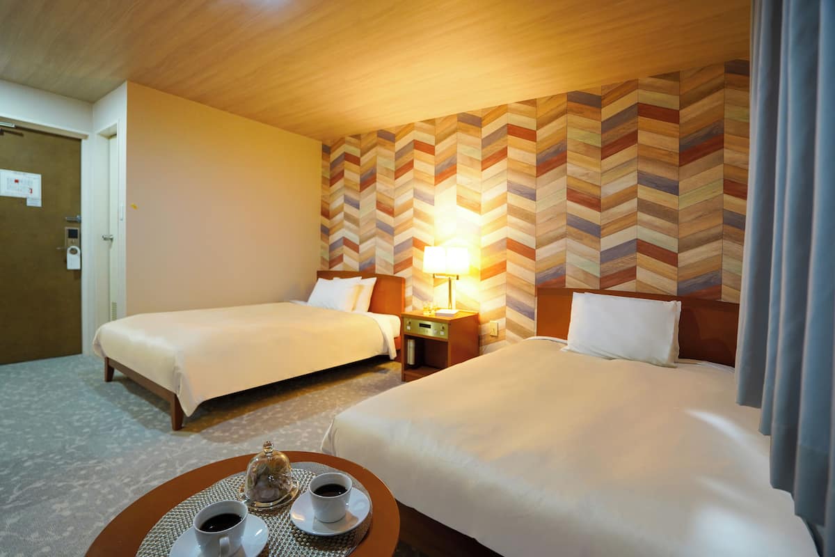 A hotel room with two beds, a nightstand with a lamp, and a tray with cups and a glass.