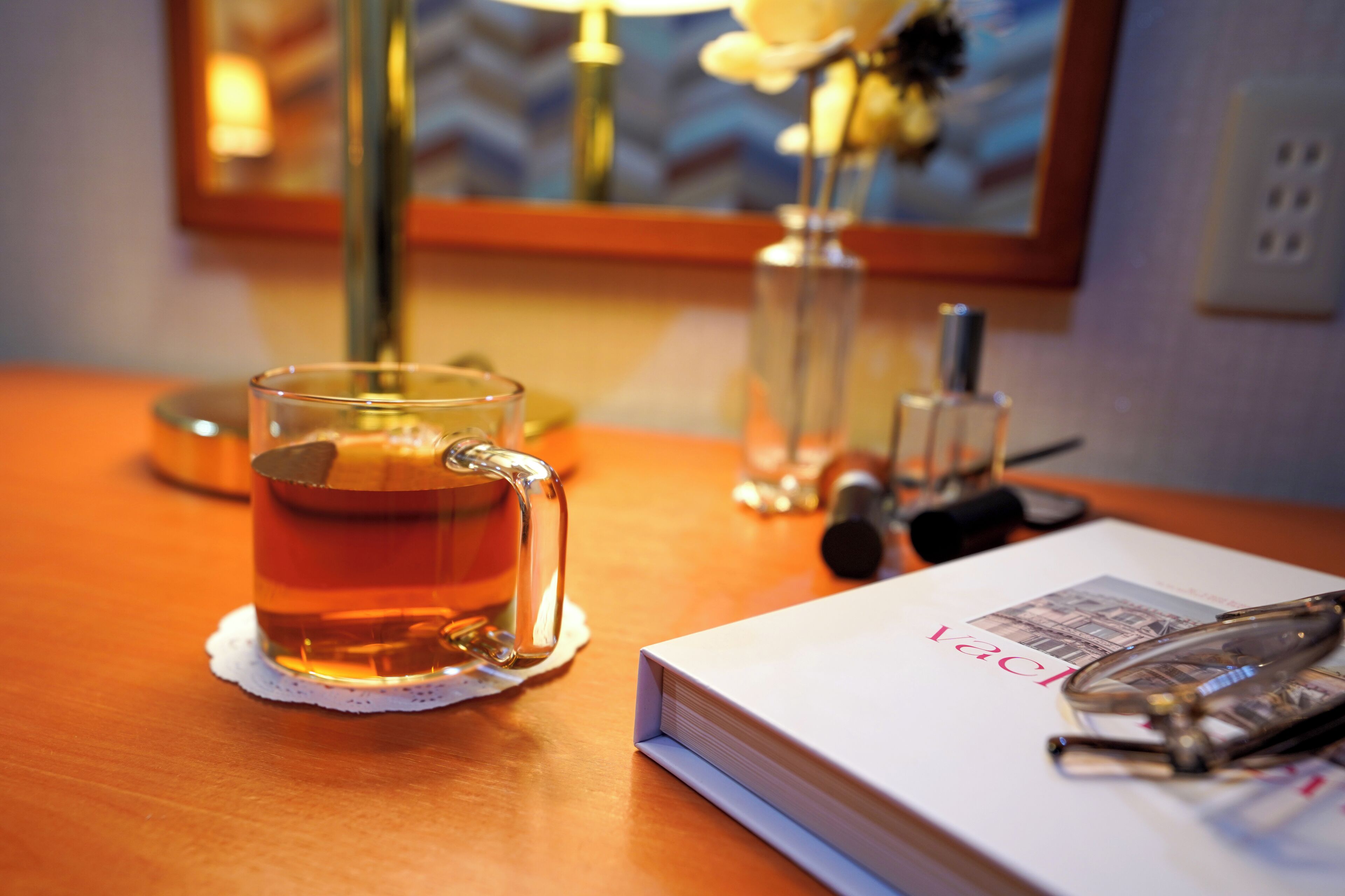 A glass of tea on a wooden table, a book, and a pair of glasses.