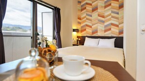 Een hotelkamer met een bed, een nachtkastje met een kopje en gebak, uitzicht op de omgeving en een muur met een zigzaagpatroon.