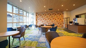 Een modern interieur met grote ramen, een muur met een chevrongpatroon en diverse zithoekopstellingen, waaronder tafels en stoelen.