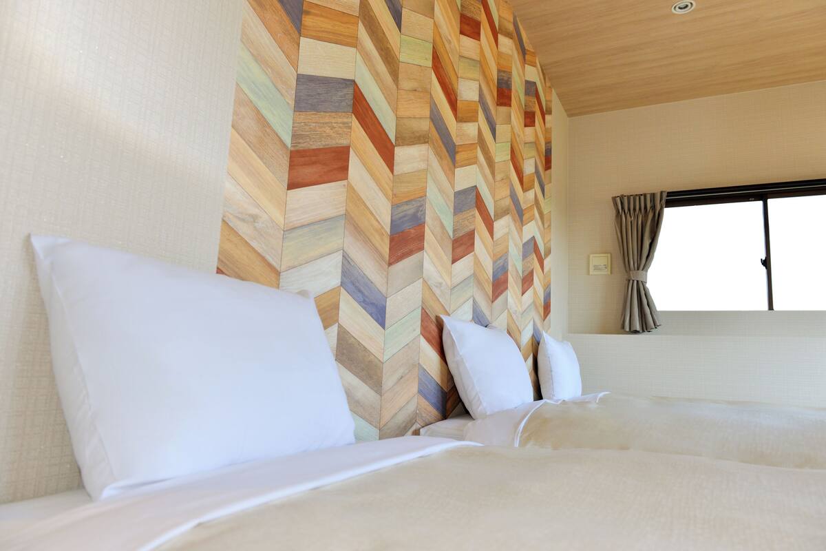 A hotel room with a large bed, a wooden herringbone-patterned wall, and a window with curtains.