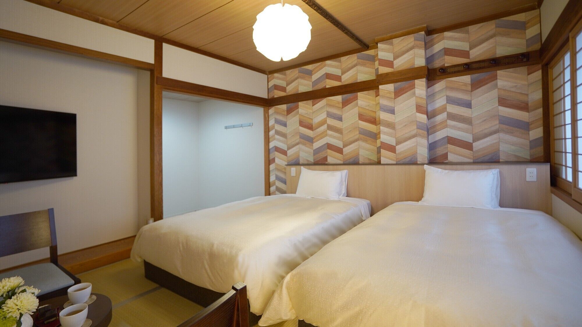 A hotel room with two beds, a TV, and a traditional Japanese-style wall design.