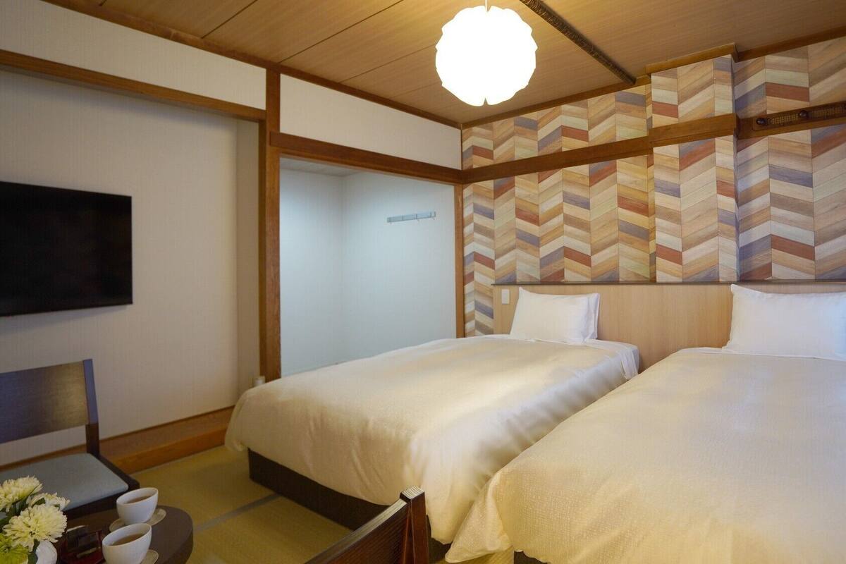 A hotel room with two beds, a TV, and a traditional Japanese-style wall design.