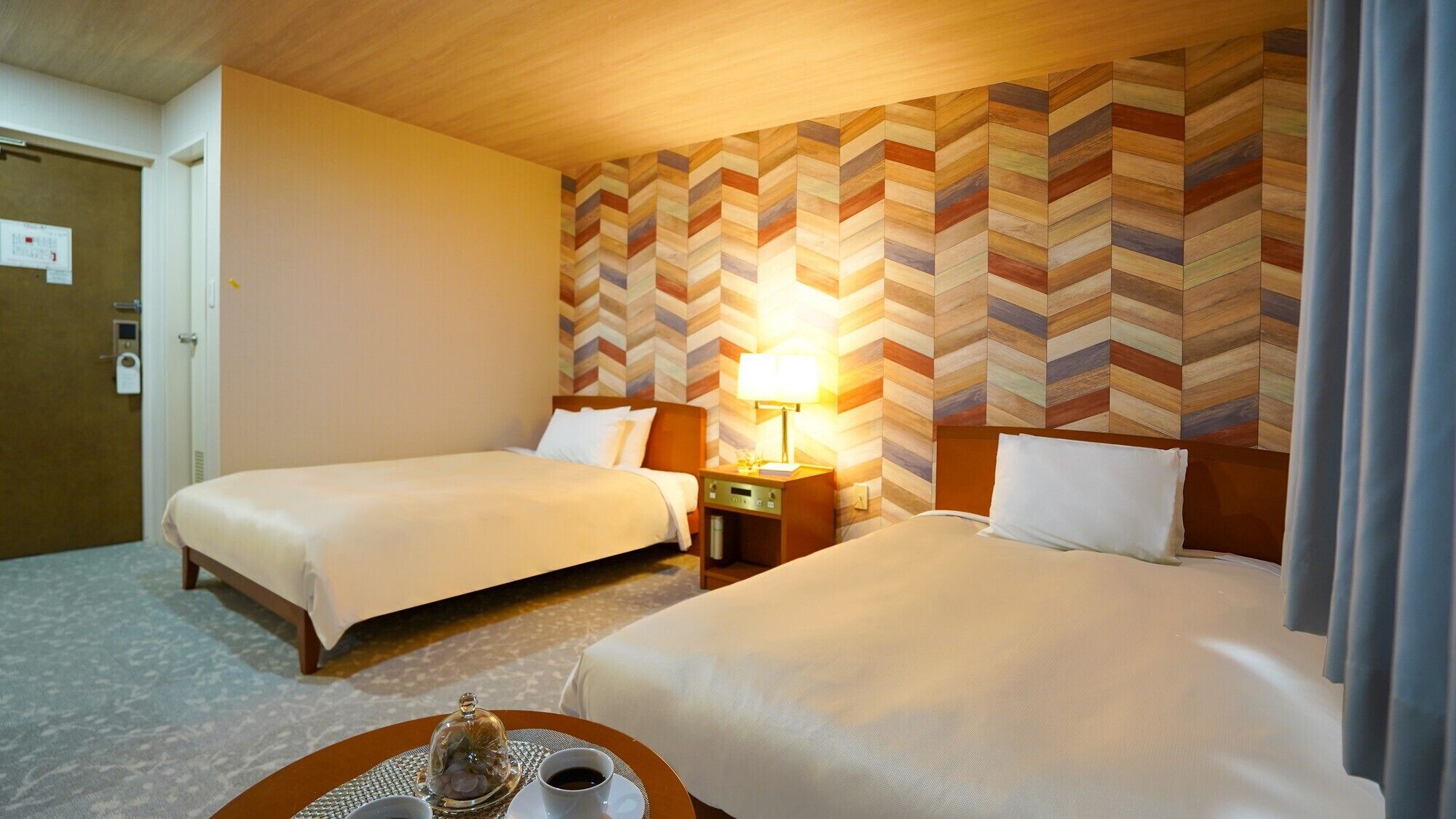 Une chambre d’hôtel avec deux lits, une table de chevet avec une lampe, un plateau avec une tasse et un verre, et un plafond en bois.