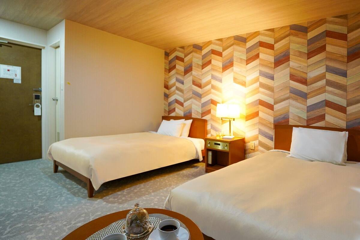 Une chambre d’hôtel avec deux lits, une table de chevet avec une lampe, un plateau avec une tasse et un verre, et un plafond en bois.