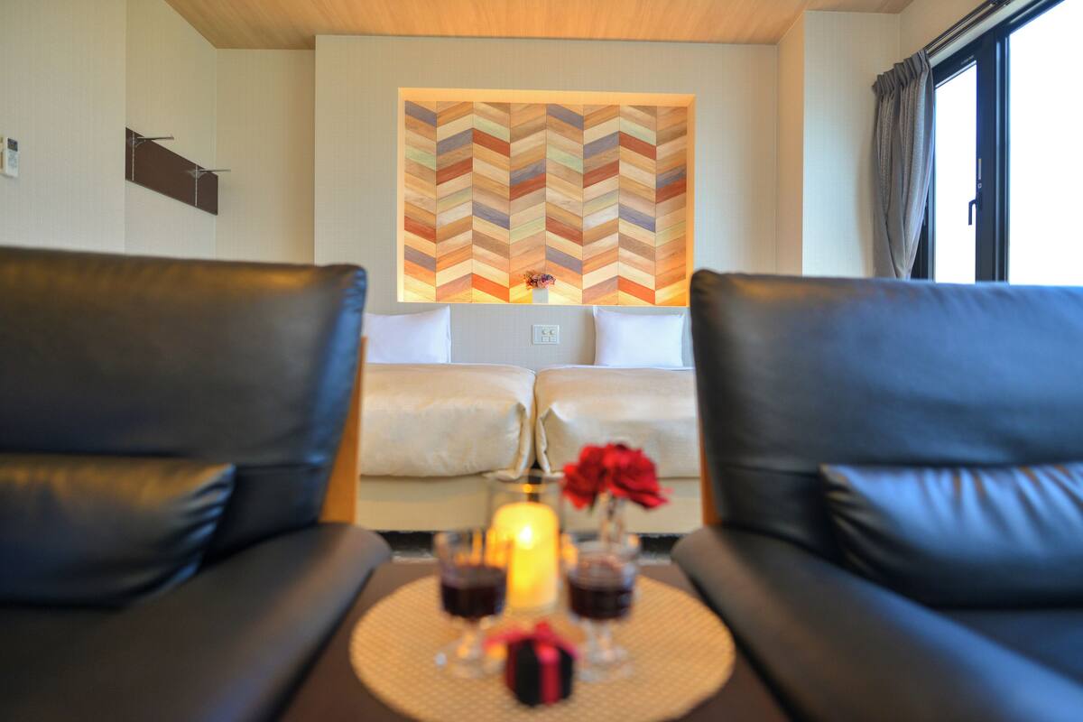 A modern living room with two black leather sofas, a central coffee table with a candle, and a decorative wall piece.