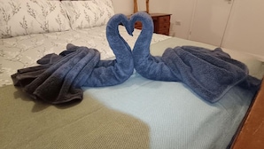 Un lit recouvert d’une couvre-lit à motifs floraux, avec deux serviettes disposées en forme de cœur.