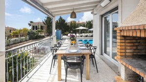 Un espacio de comedor al aire libre techado con una mesa dispuesta para seis personas, rodeada de sillas, con vistas a una piscina y un jardín.