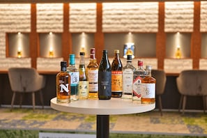 Vários copos e garrafas de bebidas sobre uma mesa, com vista para uma parede de tijolos e área de estar ao ar livre ao fundo.