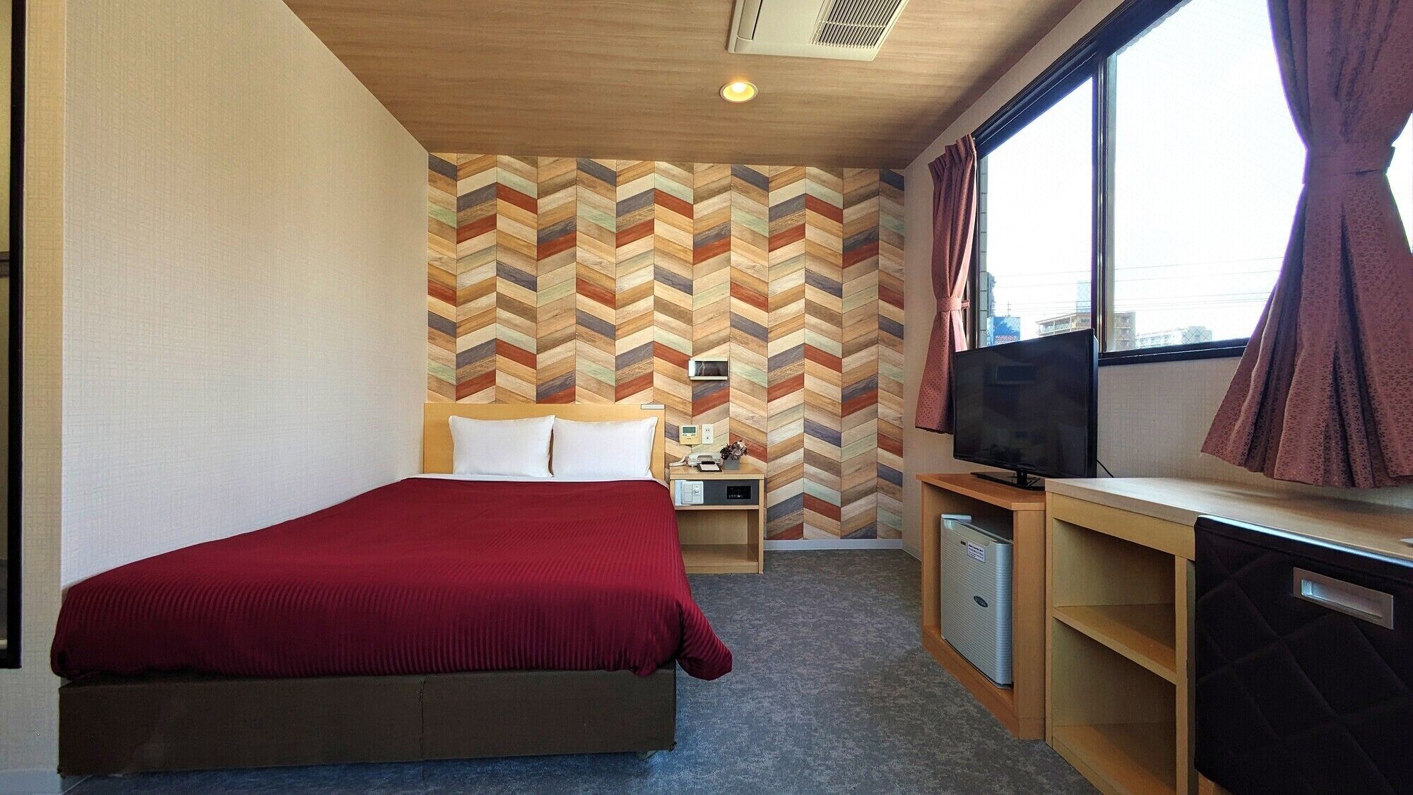 A hotel room with a bed, a TV, a desk, and a wall with a chevron pattern.