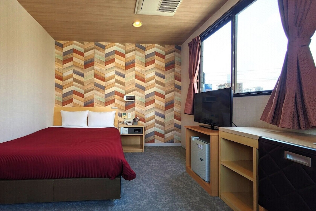 A hotel room with a bed, a TV, a desk, and a wall with a chevron pattern.