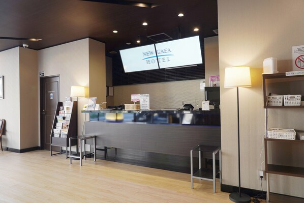 Mostrador de recepción con una pantalla digital que muestra “NEW CAEA HOTEL” y un cartel con el símbolo de prohibido fumar.