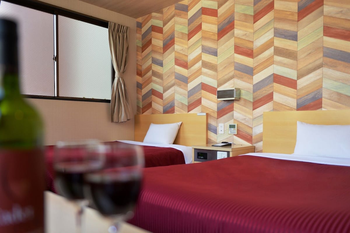 A hotel room with two beds, a minibar, and a window with curtains.