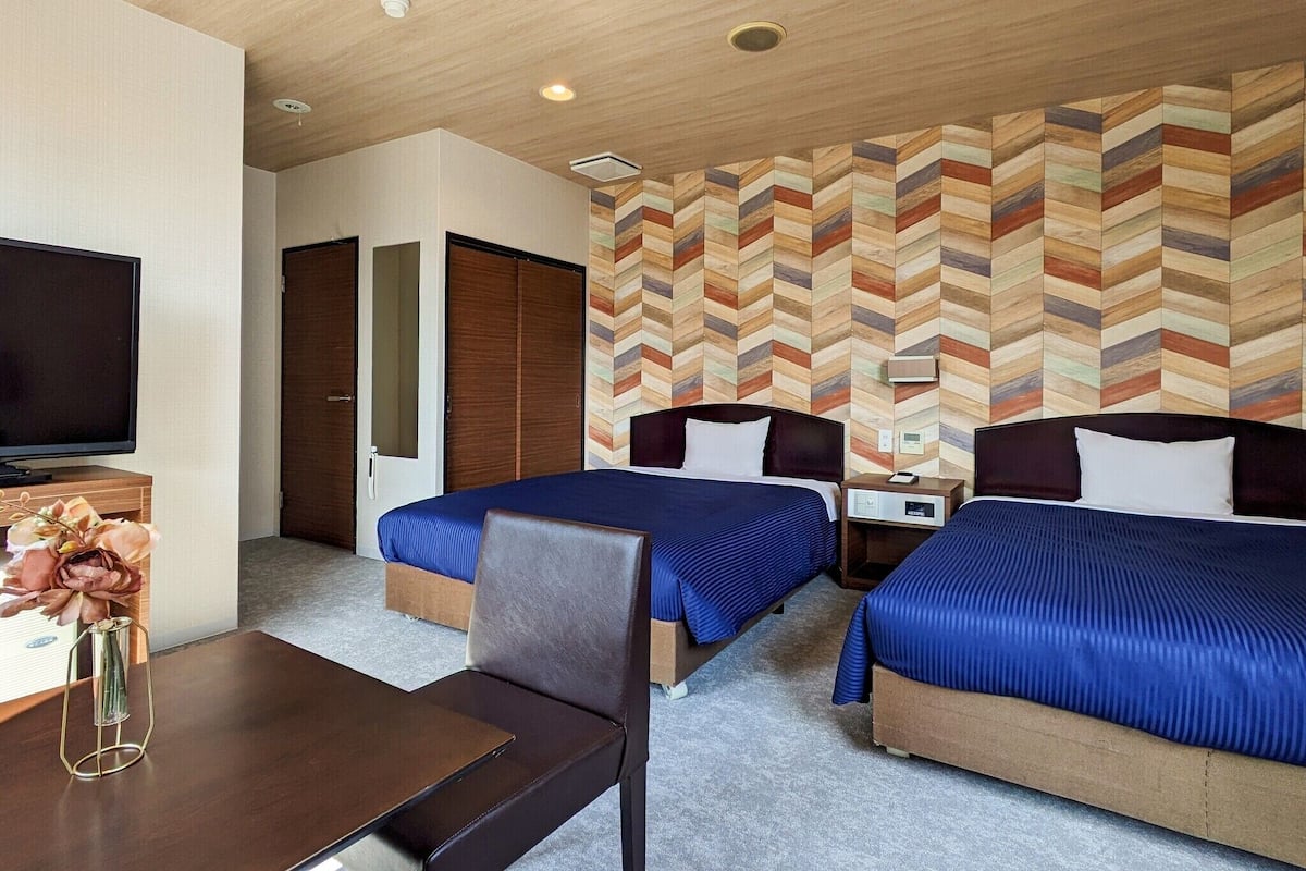 A hotel room with two beds, a TV, a desk, and a decorative vase.