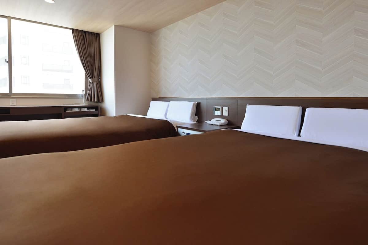 A hotel room with two beds, a desk, a chair, a telephone, and a window with curtains.