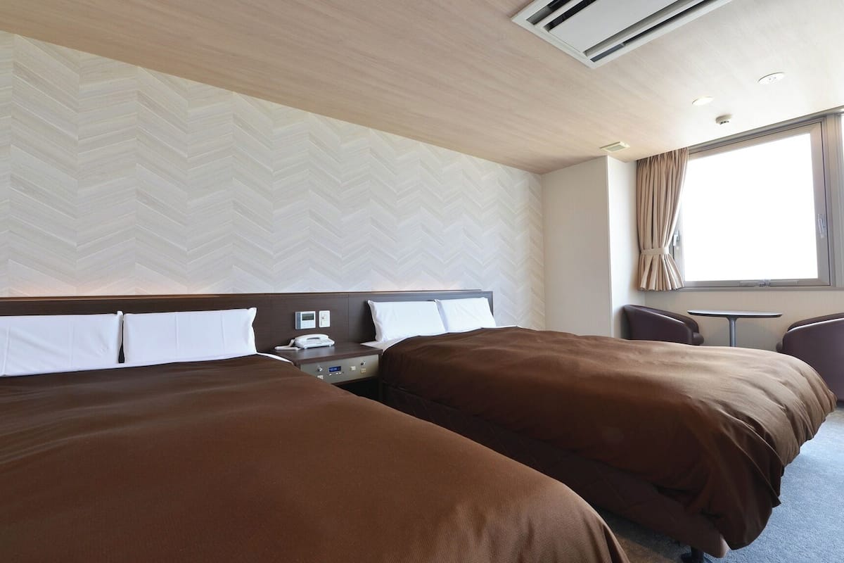 A hotel room with two beds, a desk, and a chair.