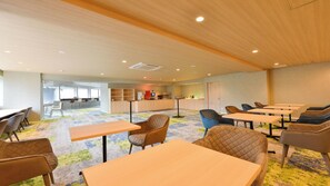 Une salle de conférence moderne, équipée de tables et de chaises, d’un coin cuisine et d’une grande fenêtre.