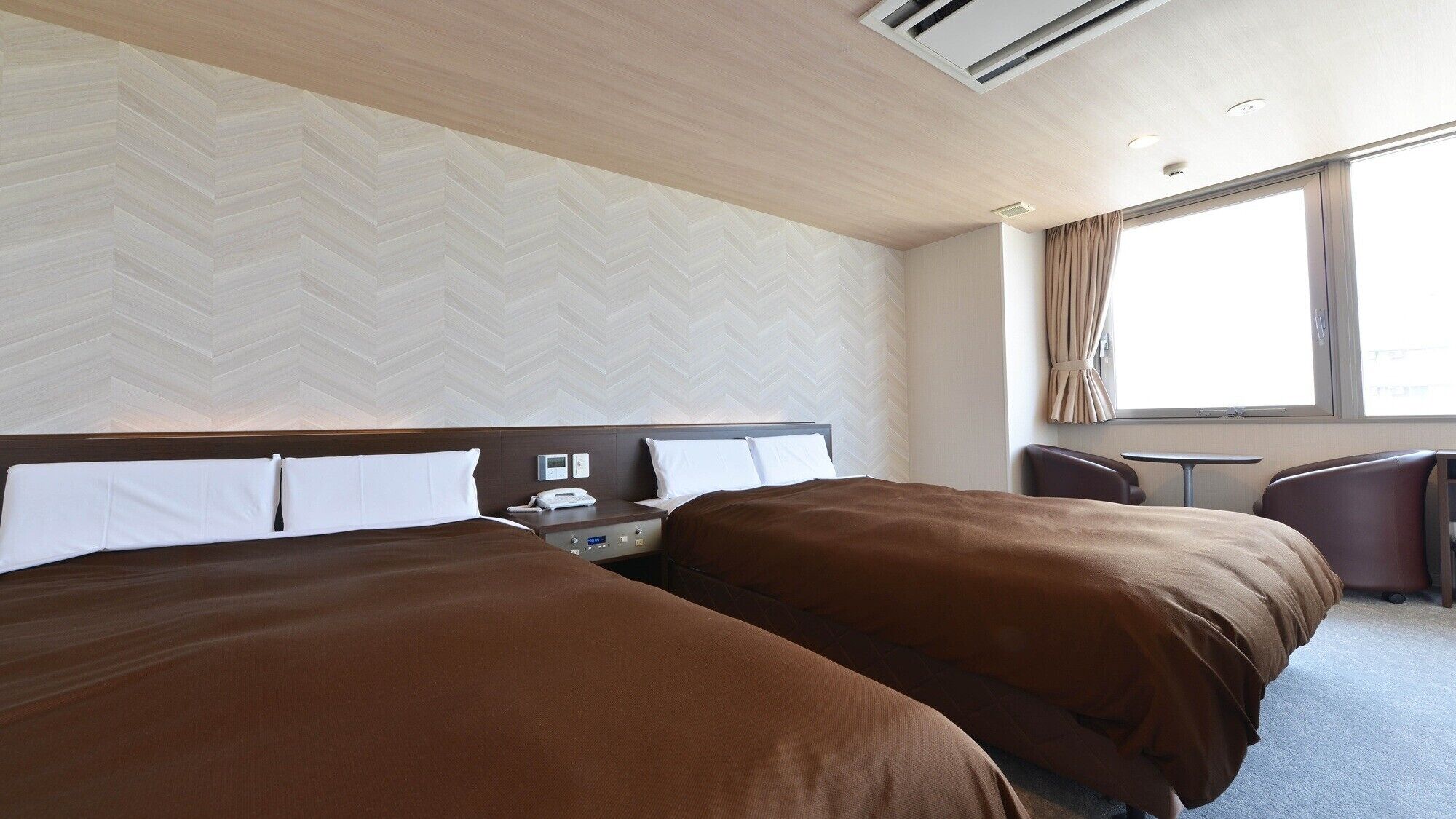 Ein Hotelzimmer mit zwei Betten, einem Schreibtisch, einem Stuhl und einem Vorhangfenster.