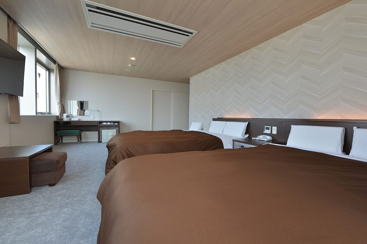 A hotel room with two beds, a desk, a chair, a TV, and a large window.
