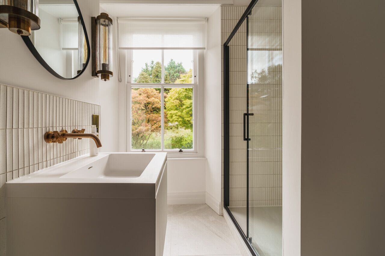 Een moderne badkamer met een groot wit bad, een douchecabine van glas en een raam met uitzicht op bomen.