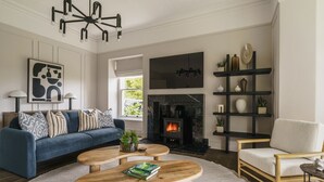 Una sala de estar con un sofá azul, una mesa de centro de madera, chimenea y estantería.