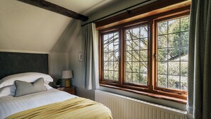 A bedroom with a large window, a bed with a yellow blanket, and a wooden headboard.