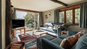 A cozy living room with a large TV, comfortable sofas, a coffee table, and a rustic wooden beam ceiling.