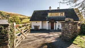 A white cottage with a stone entrance, a wooden gate, and a stone wall.