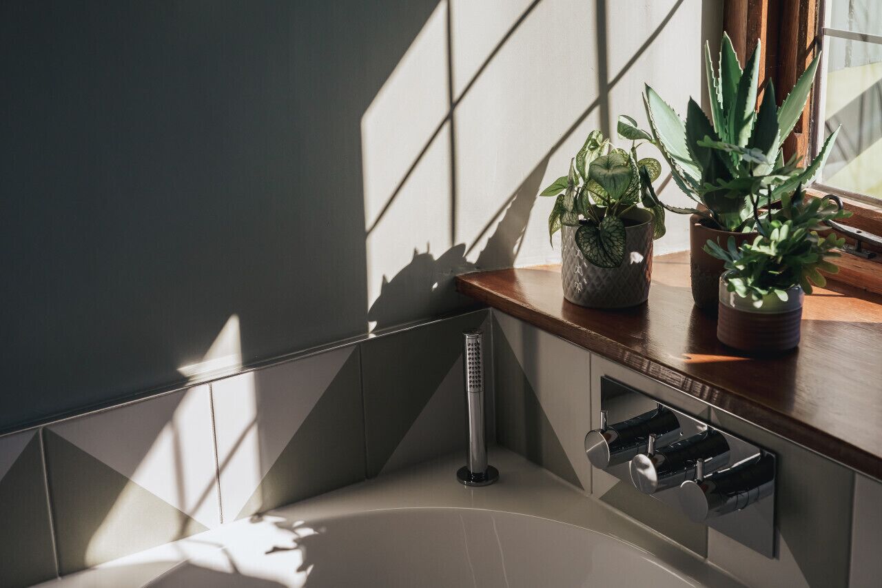Un baño moderno con bañera, ducha y una ventana que deja pasar la luz del sol, proyectando sombras en la pared.