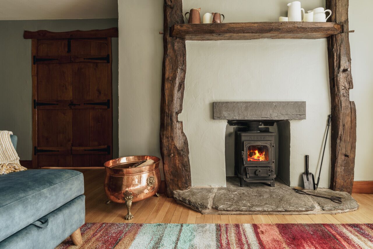 Una sala de estar acogedora con chimenea, un sofá azul, una olla de cobre y un estante rústico de madera sobre la chimenea.